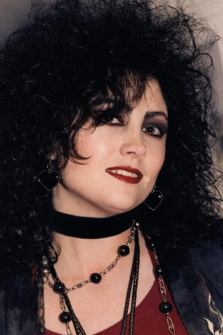 Woman with curly black hair and dark makeup wearing gothic jewelry.