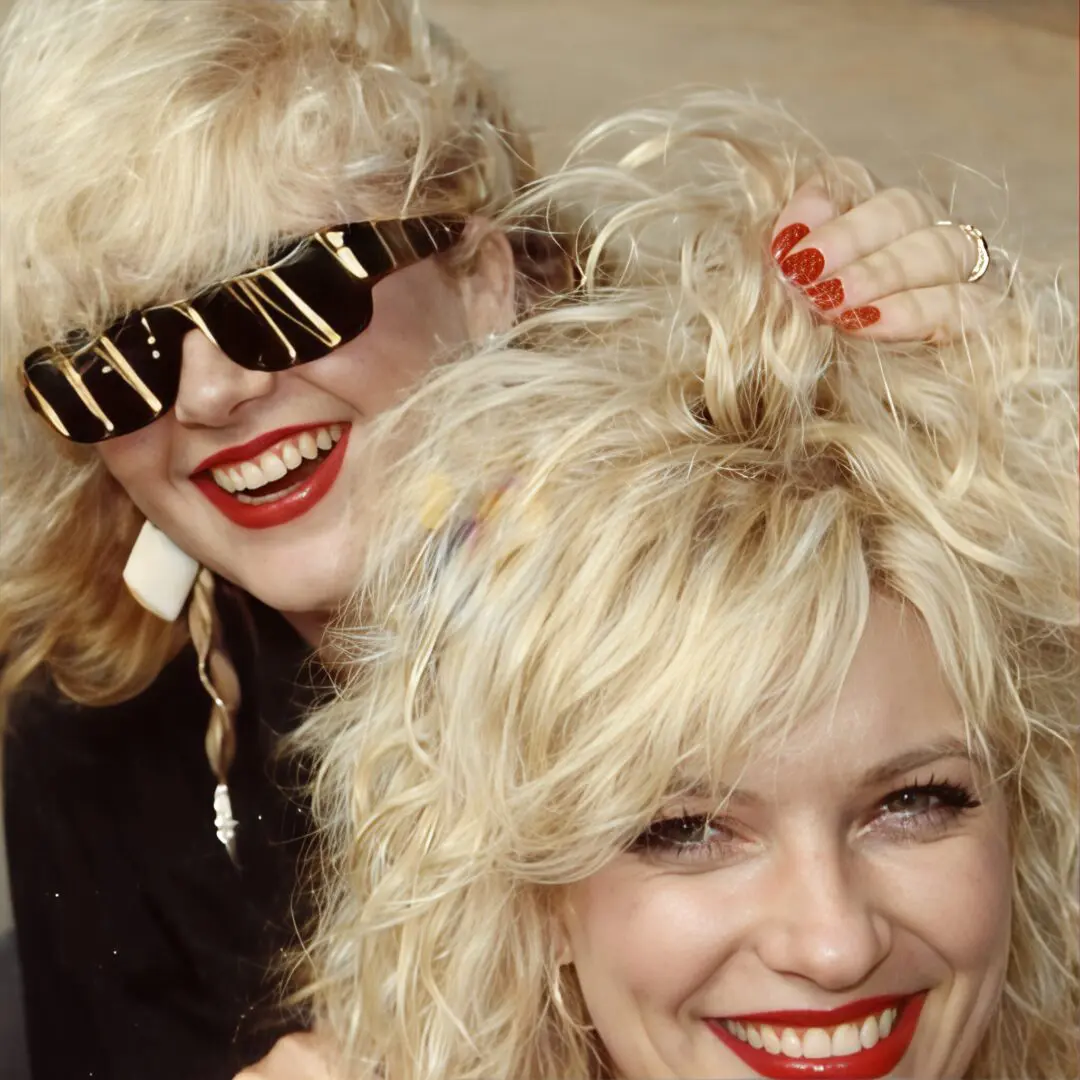 Two women with big curly blonde hair and bright smiles.