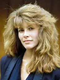 Woman with voluminous, wavy hair, smiling slightly.