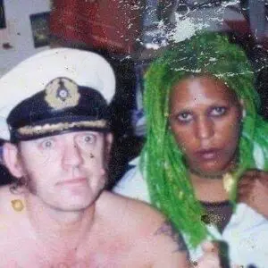 Two people: green-haired person and man in cap