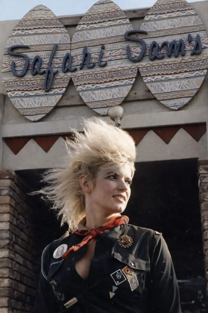 Blonde woman with spiky hair by sign